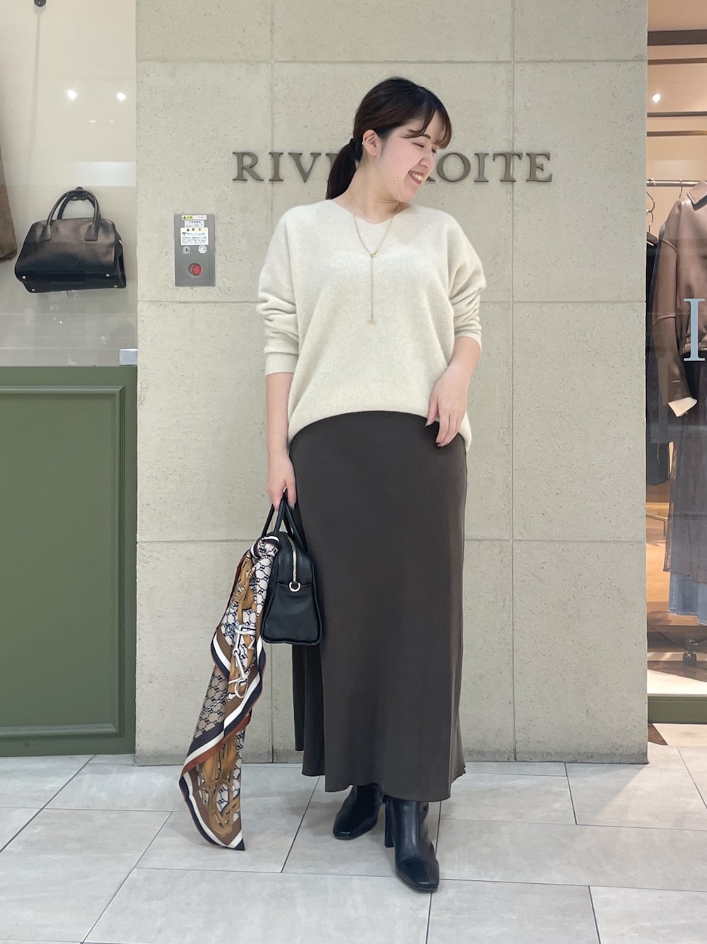ベージュ系のニット/セーター、ブラウン系のスカート、ブラック系のボストンバッグを着用したレディースの秋コーディネートの1枚目の写真