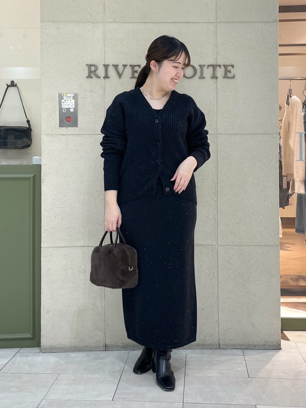 ブラック系のカーディガン/ボレロ、ブラック系のスカート、ブラウン系のボストンバッグを着用したレディースの秋コーディネートの1枚目の写真