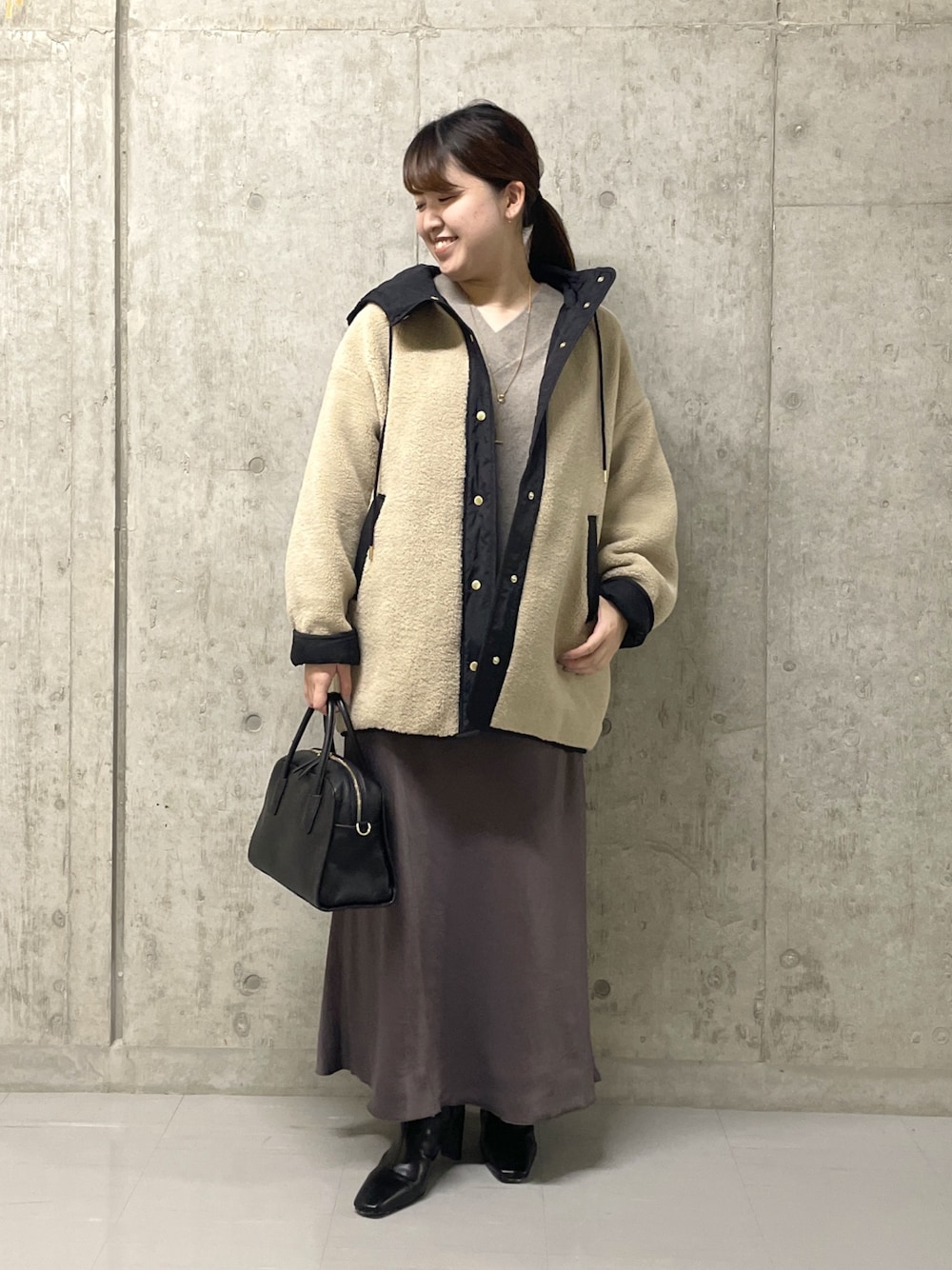 ブラウン系のスカート、ブラック系のボストンバッグ、ブラック系のブーツを着用したレディースの秋コーディネートの1枚目の写真