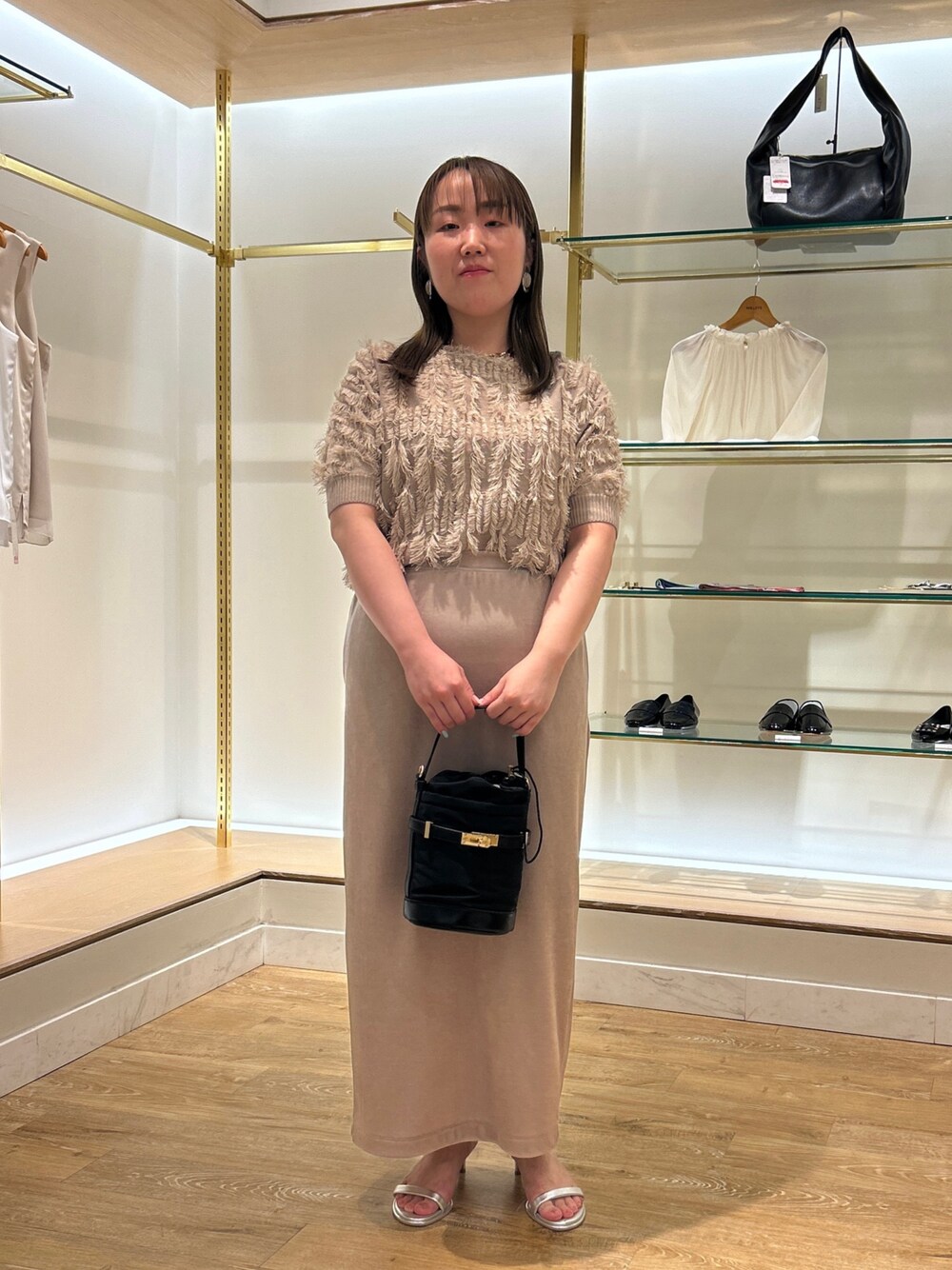 ベージュ系のニット/セーター、ベージュ系のスカート、ブラック系のショルダーバッグを着用したレディースの夏コーディネートの1枚目の写真