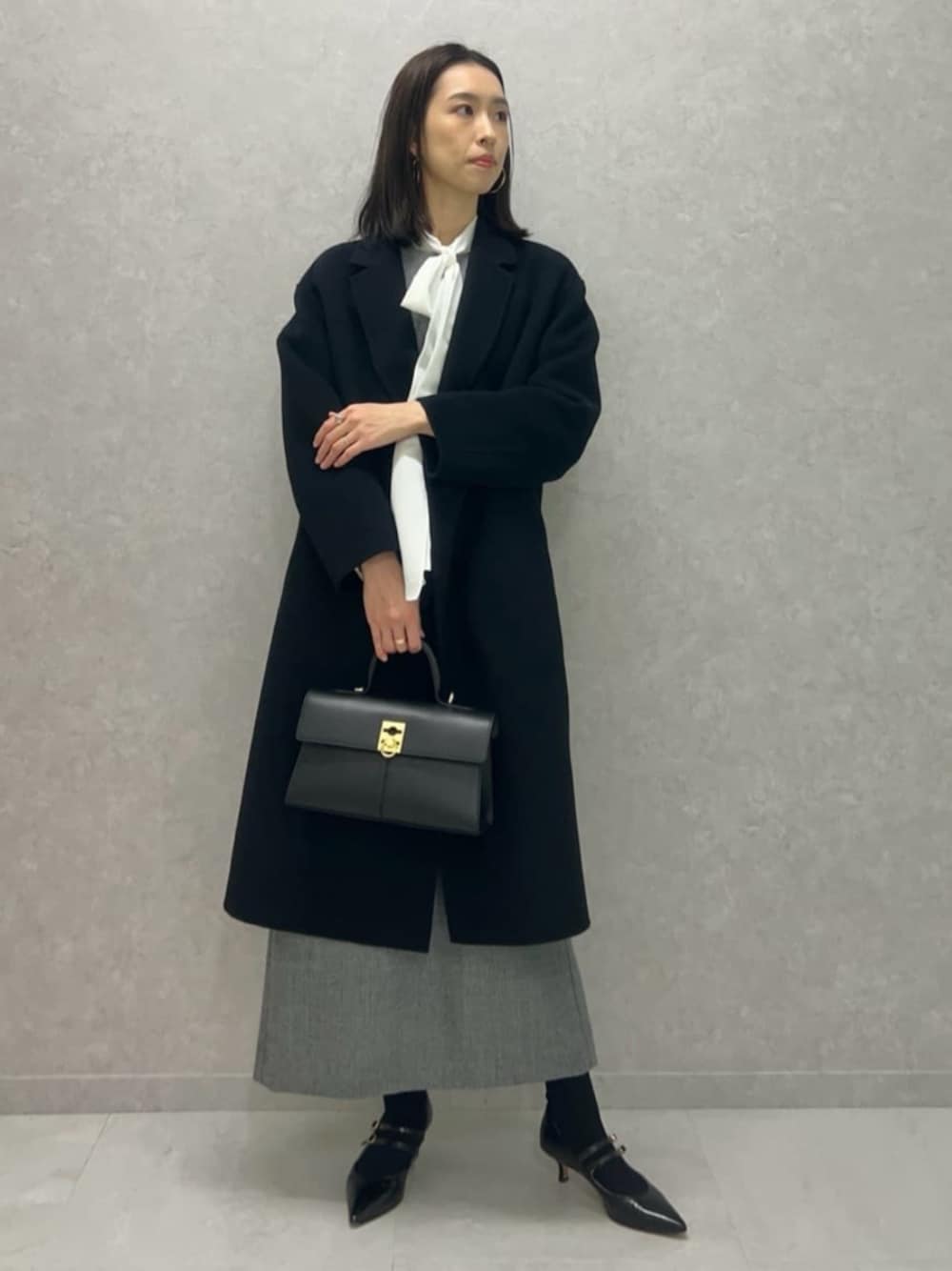 ブラック系のパンプス、ブラック系のチェスターコート、ホワイト系のシャツ/ブラウスを着用したレディースの冬コーディネートの1枚目の写真
