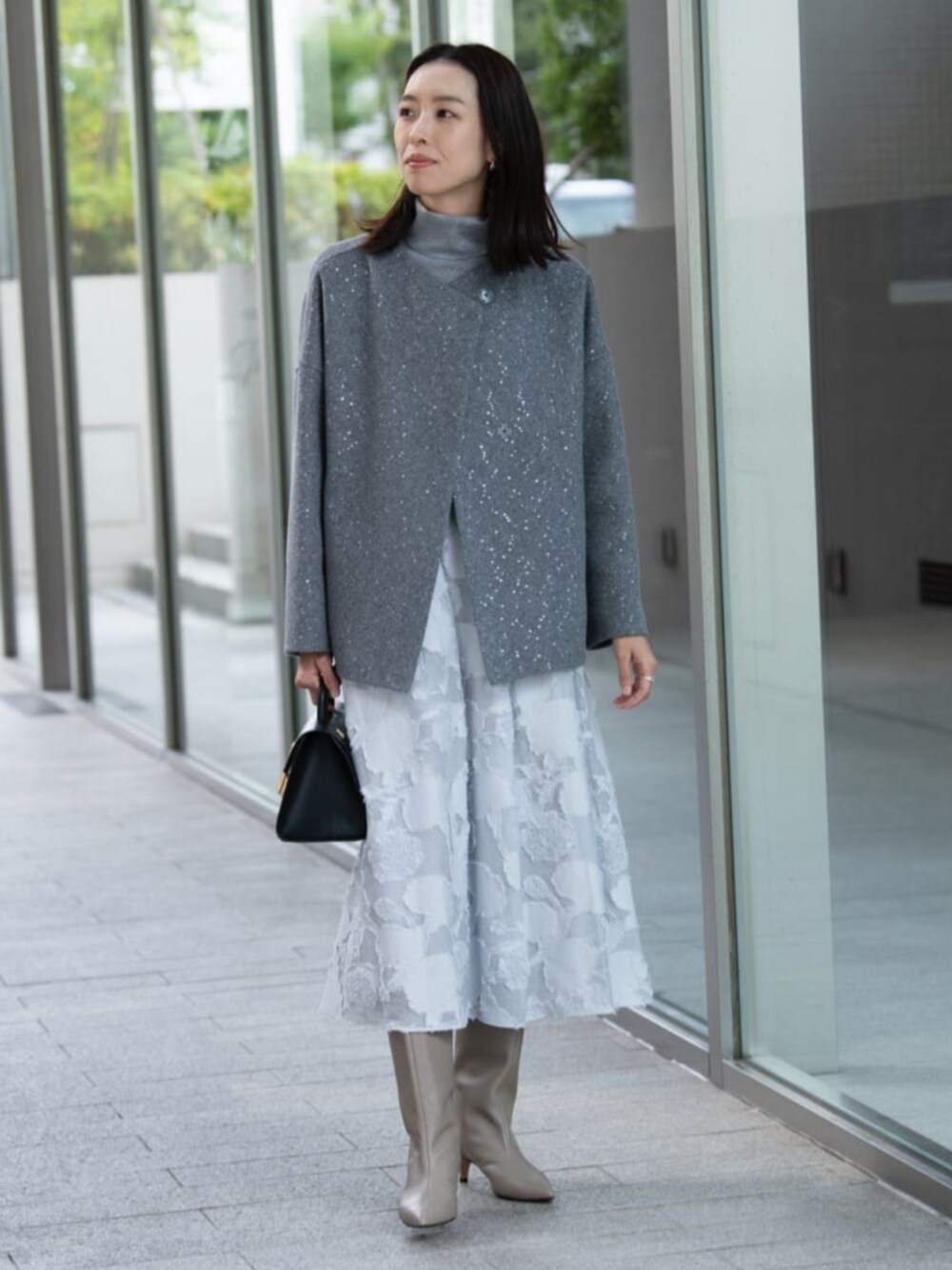 グレー系のノーカラーコート、グレー系のニット/セーター、ブルー系のスカートを着用したレディースの秋コーディネートの1枚目の写真