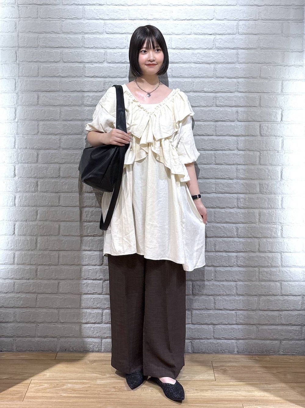 ブラック系のパンプス、ブラウン系のスラックス、ブラック系のショルダーバッグを着用したレディースの夏コーディネートの1枚目の写真