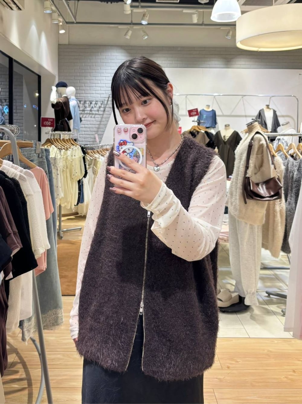 ブラック系のスカート、ブラウン系のベスト、ホワイト系のTシャツ/カットソーを着用したレディースの秋コーディネートの1枚目の写真