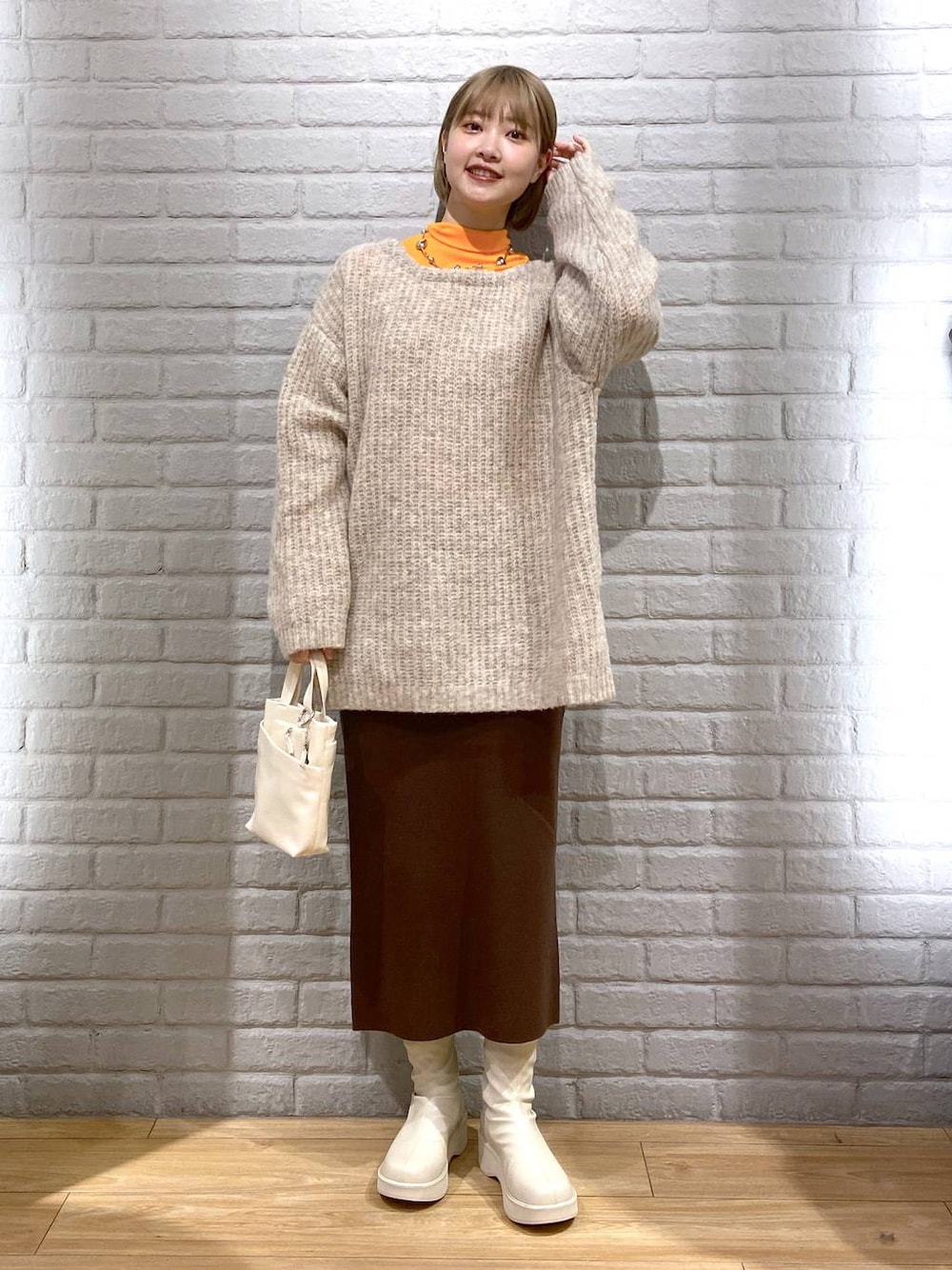 オレンジ系のTシャツ/カットソー、ホワイト系のブーツ、ブラウン系のスカートを着用したレディースの冬コーディネートの1枚目の写真