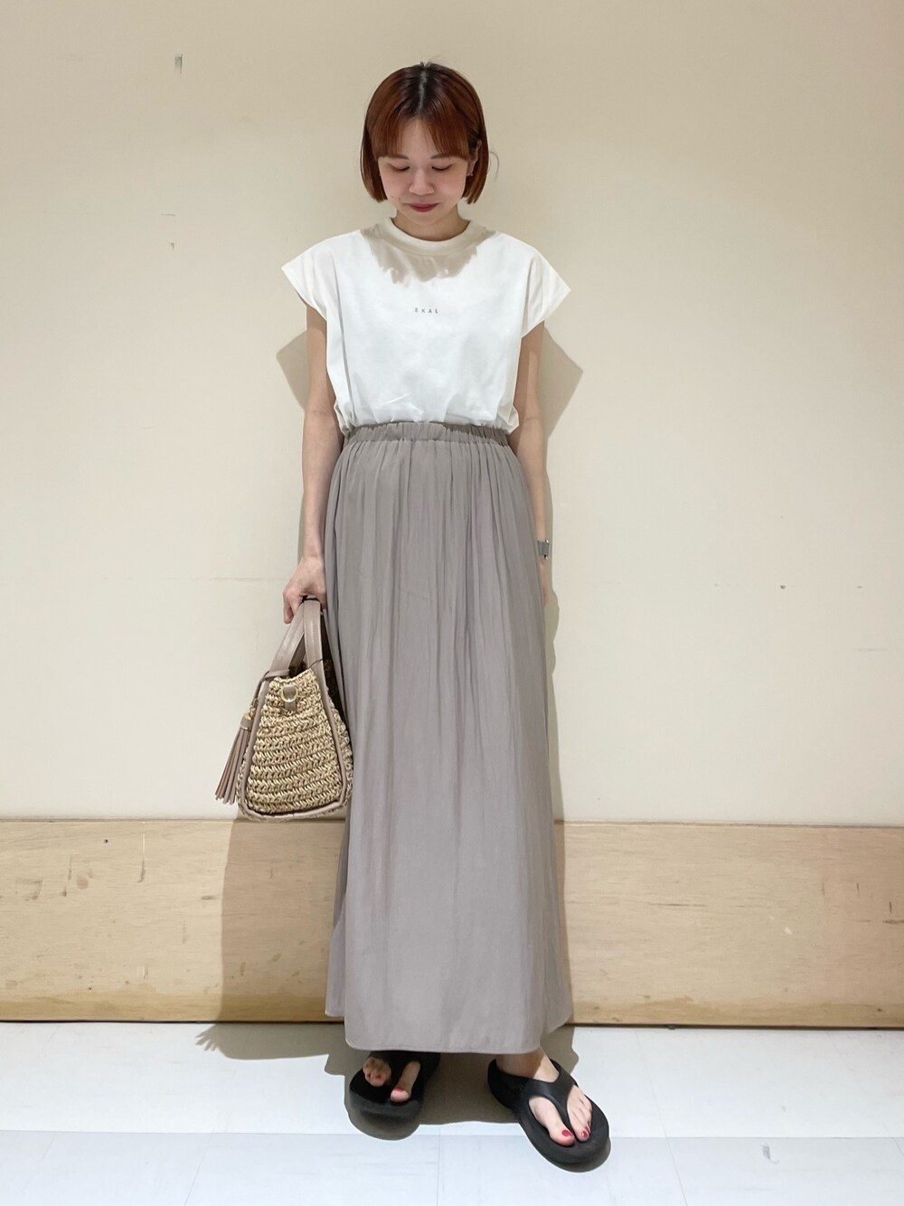 グレー系のスカート、ホワイト系のTシャツ/カットソー、ベージュ系のかごバッグを着用したレディースの春コーディネートの1枚目の写真