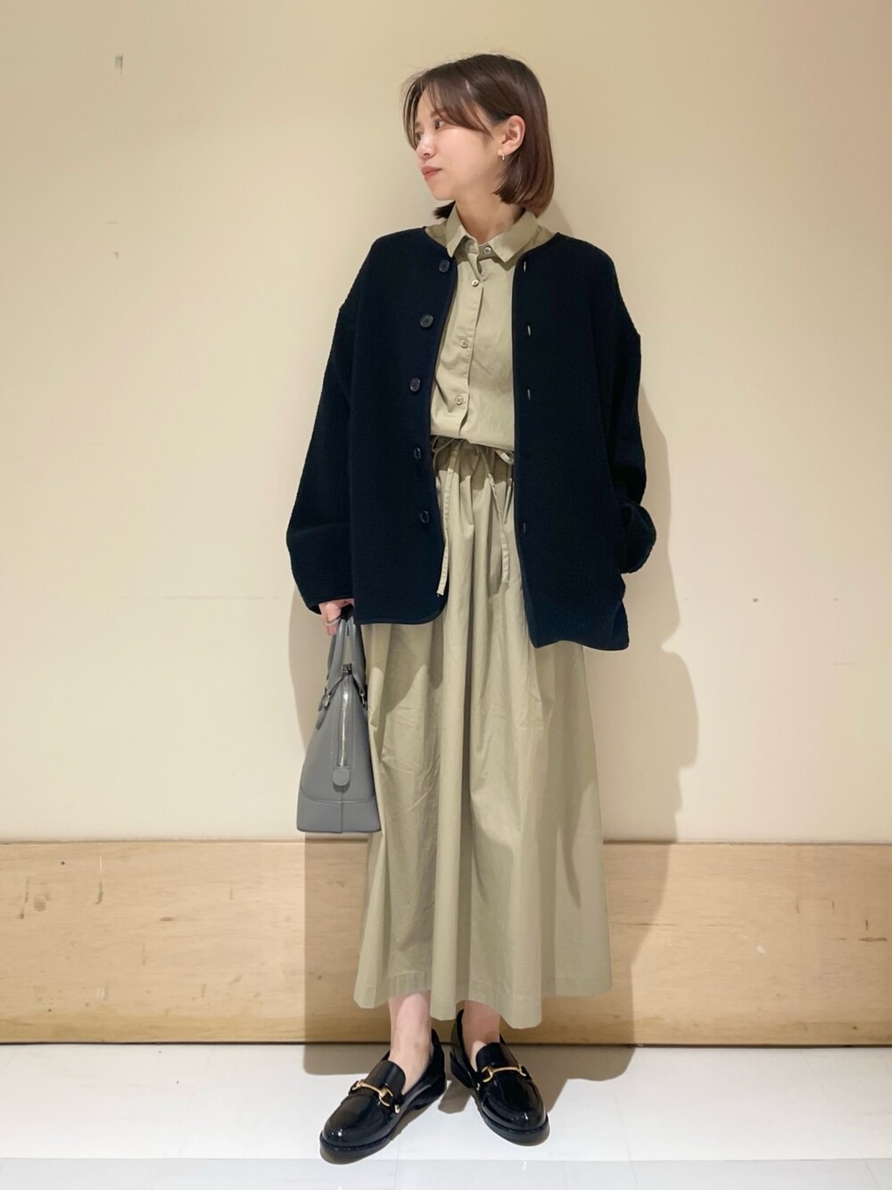 グレー系のショルダーバッグ、ブラック系のノーカラージャケット、ベージュ系のワンピースを着用したレディースの秋コーディネートの1枚目の写真