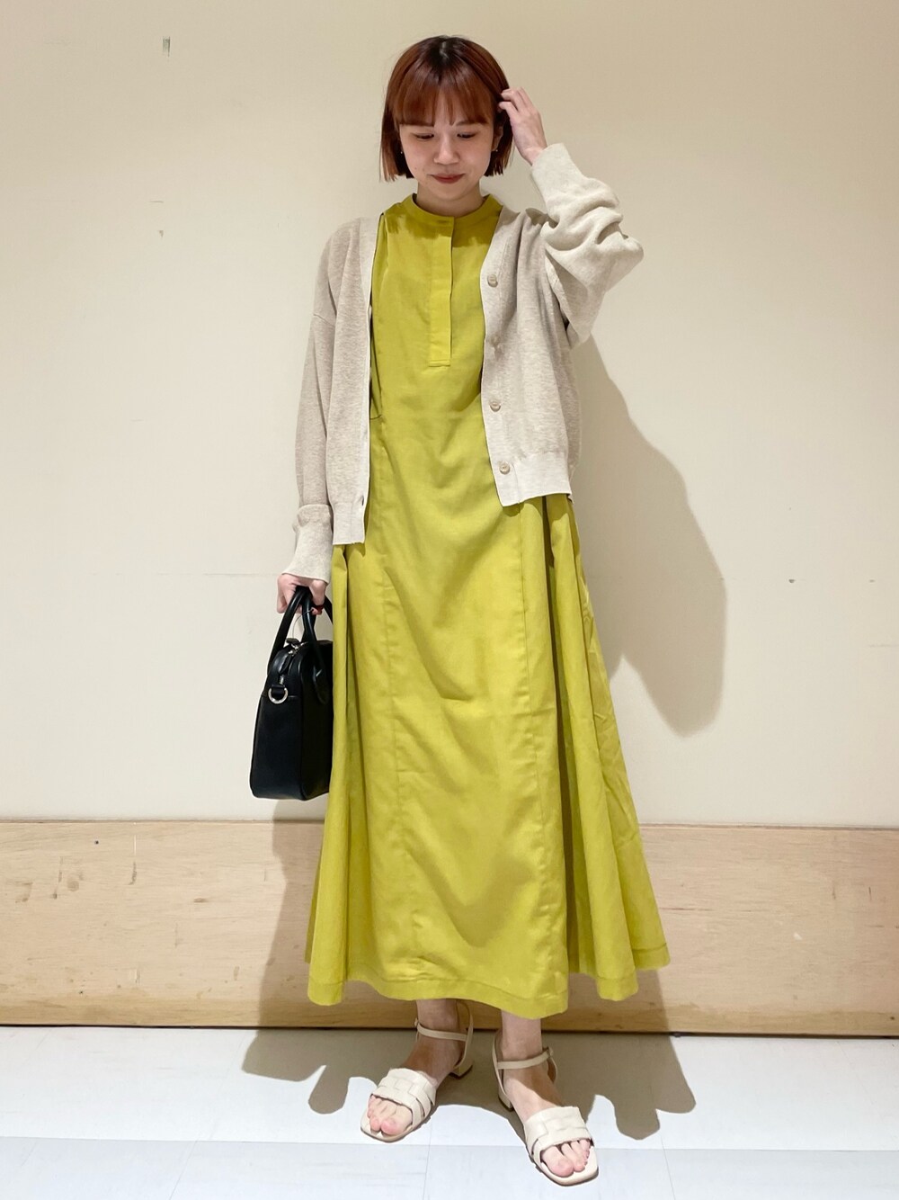 イエロー系のワンピース、ベージュ系のニット/セーター、ブラック系のショルダーバッグを着用したレディースの春コーディネートの1枚目の写真