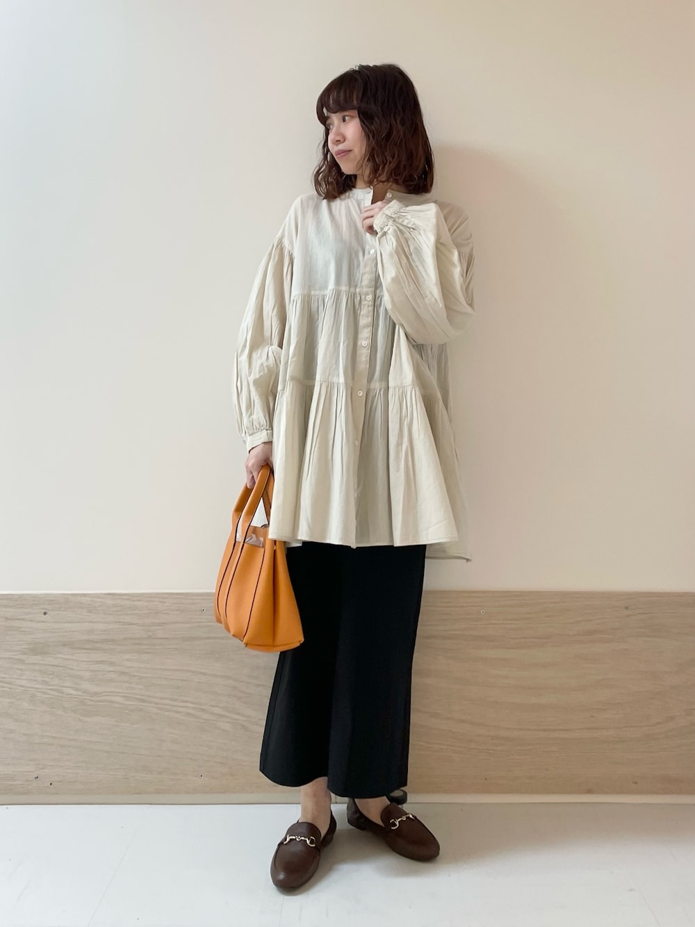 ブラック系のスカート、ホワイト系のチュニックを着用したレディースの春コーディネートの1枚目の写真