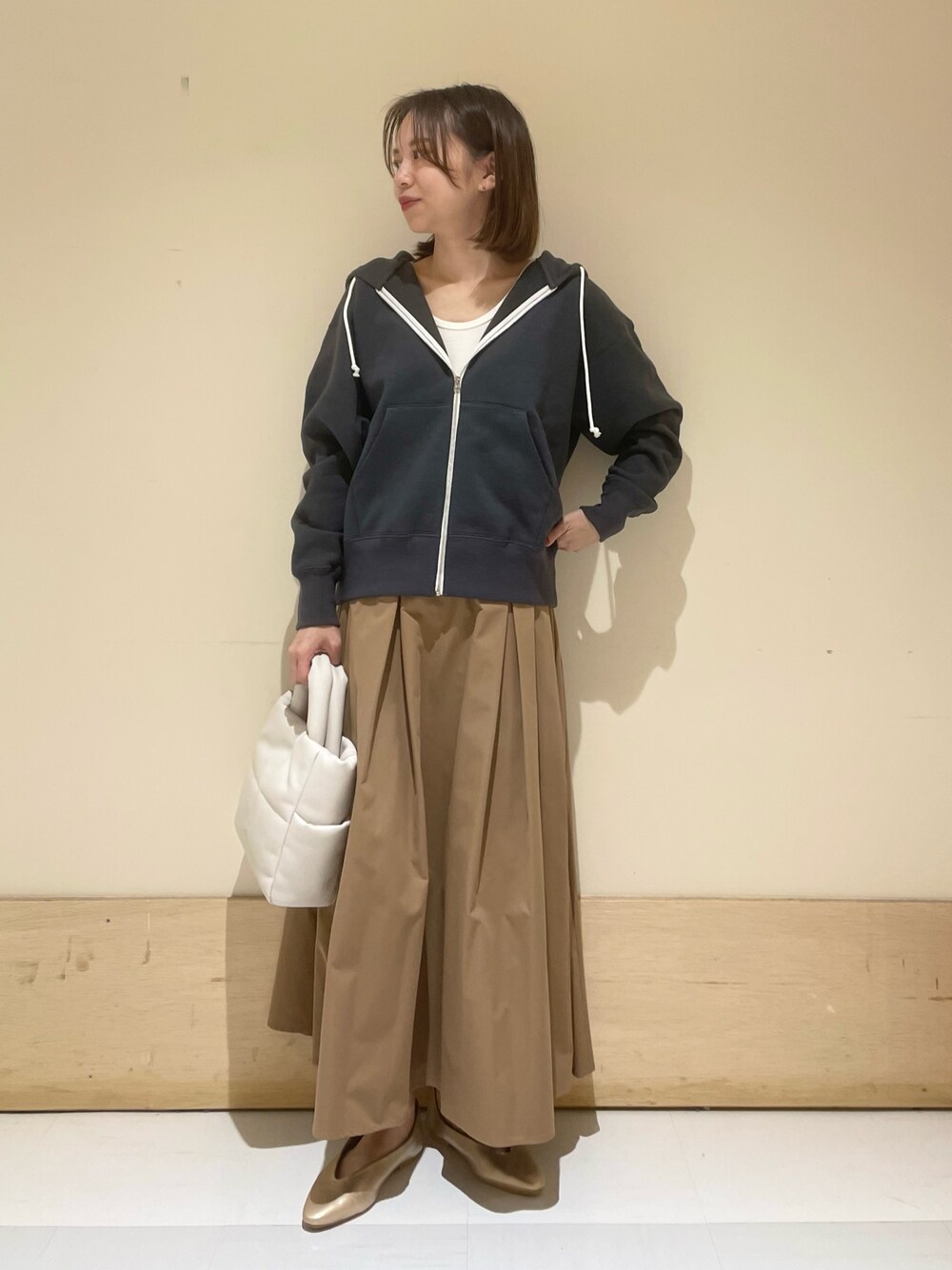 ゴールド系のパンプス、ホワイト系のトートバッグ、ベージュ系のスカートを着用したレディースの秋コーディネートの1枚目の写真