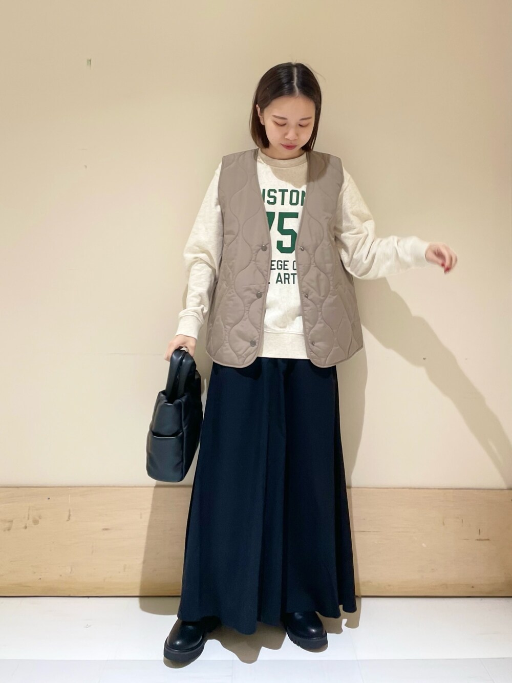 ブラック系のスカート、ブラック系のブーツ、ブラウン系のダウンベストを着用したレディースの秋コーディネートの1枚目の写真