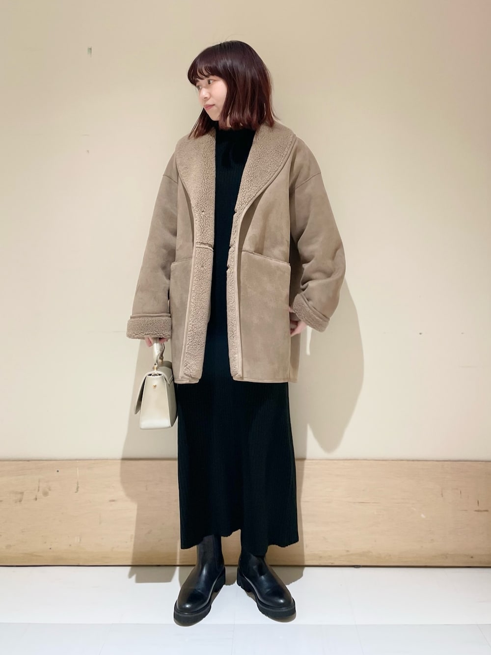 グレー系のムートンコート、ブラック系のワンピース、ゴールド系のショルダーバッグを着用したレディースの冬コーディネートの1枚目の写真