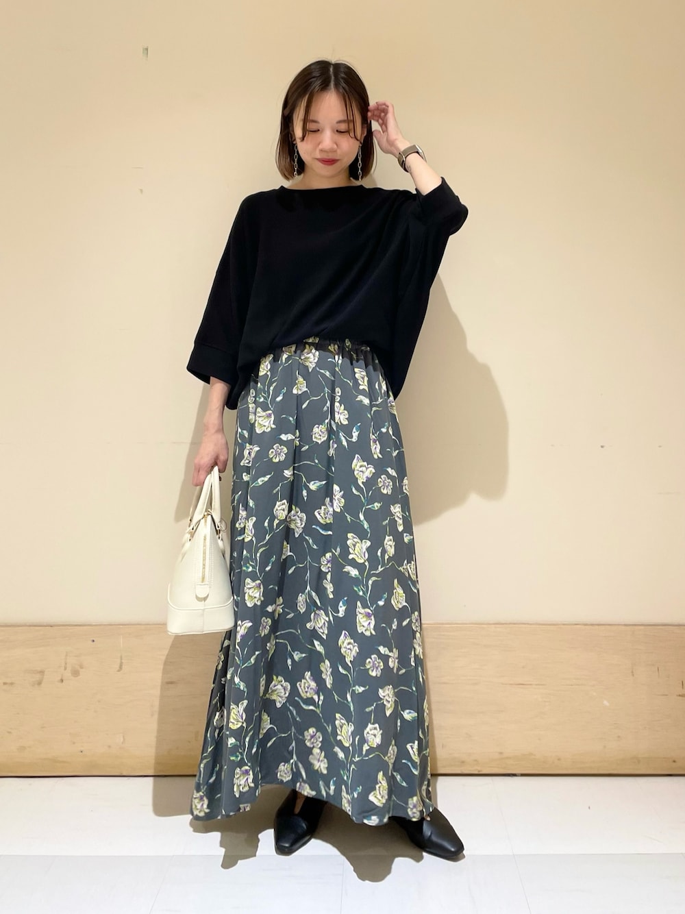 グレー系のスカート、ホワイト系のショルダーバッグ、ブラック系のパンプスを着用したレディースの秋コーディネートの1枚目の写真