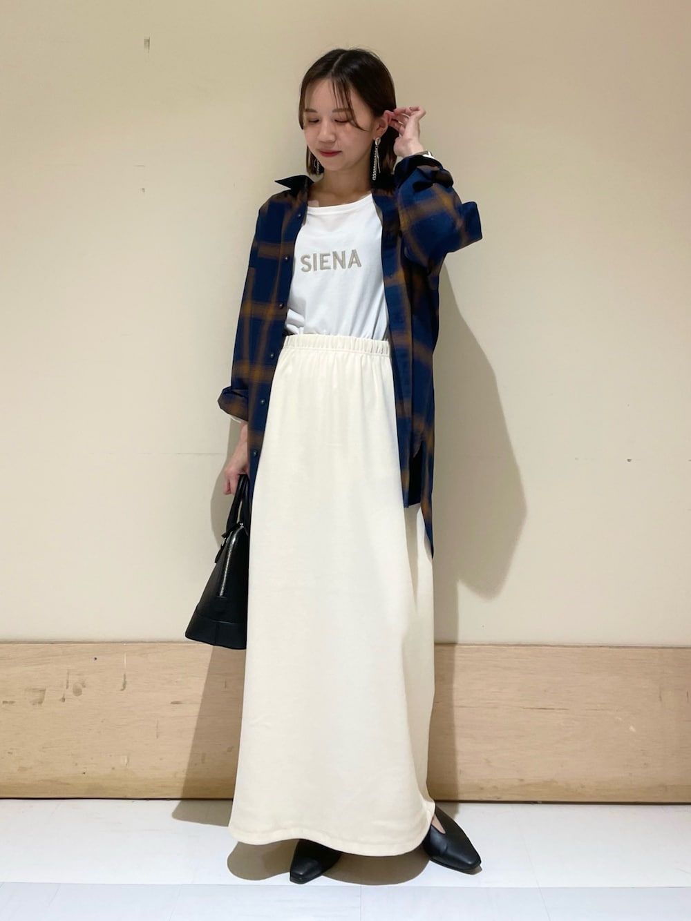 ベージュ系のスカート、ブラック系のパンプス、ブラック系のショルダーバッグを着用したレディースの秋コーディネートの1枚目の写真