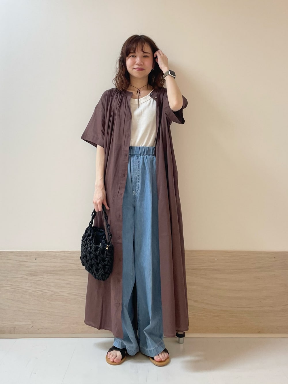 ブルー系のデニムパンツ、ブラック系のサンダル、ブラウン系のワンピースを着用したレディースの春コーディネートの1枚目の写真