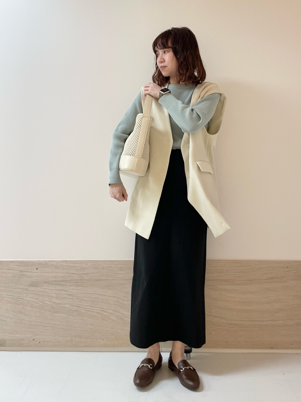 グリーン系のニット/セーター、ホワイト系のその他アウター、ブラック系のスカートを着用したレディースの春コーディネートの1枚目の写真