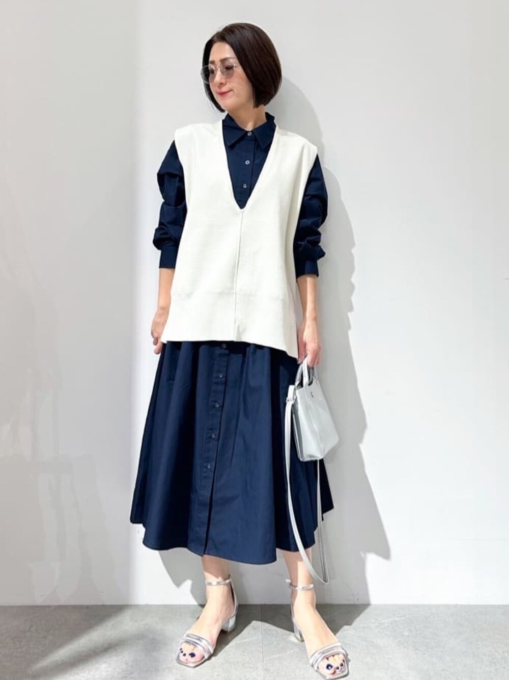 ホワイト系のベスト、ブルー系のワンピース、シルバー系のサンダルを着用したレディースの春コーディネートの1枚目の写真