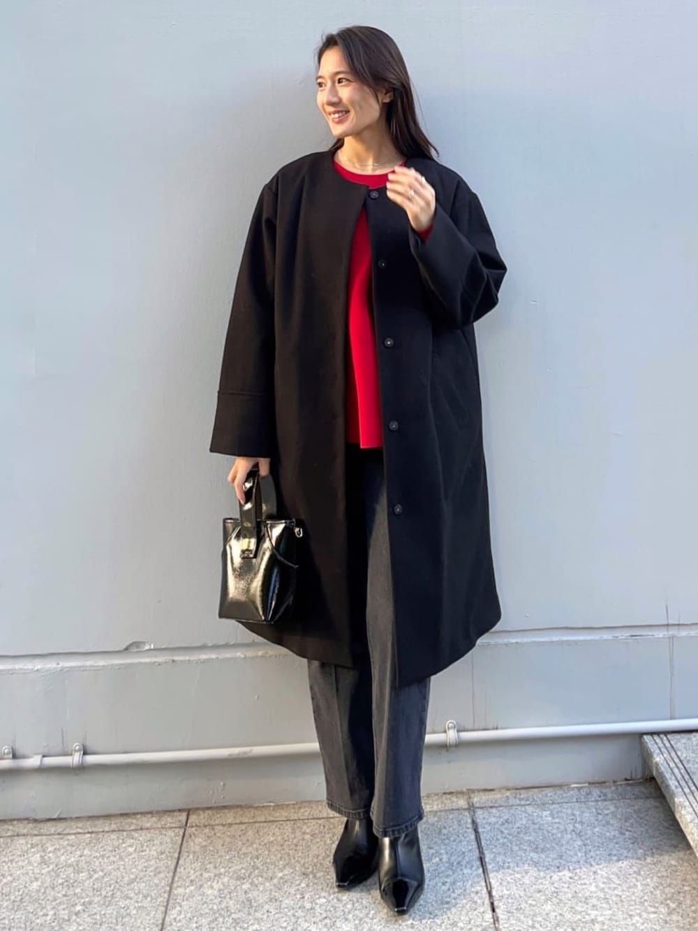 レッド系のニット/セーター、ブラック系のノーカラーコート、ブラック系のデニムパンツを着用したレディースの冬コーディネートの1枚目の写真