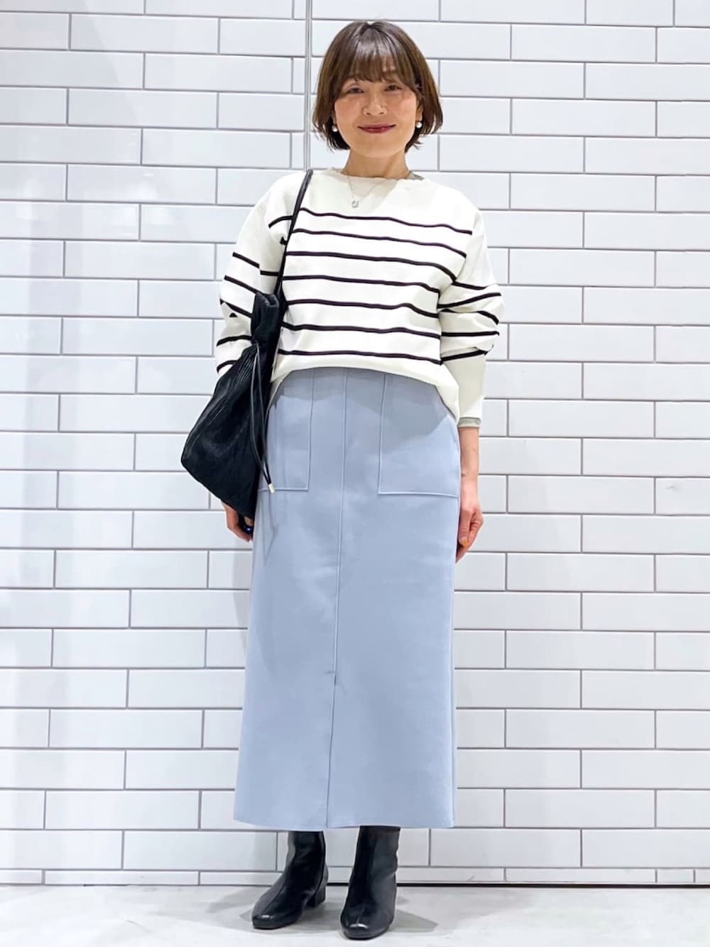 ホワイト系のニット/セーター、ブルー系のスカート、ブラック系のトートバッグを着用したレディースの冬コーディネートの1枚目の写真
