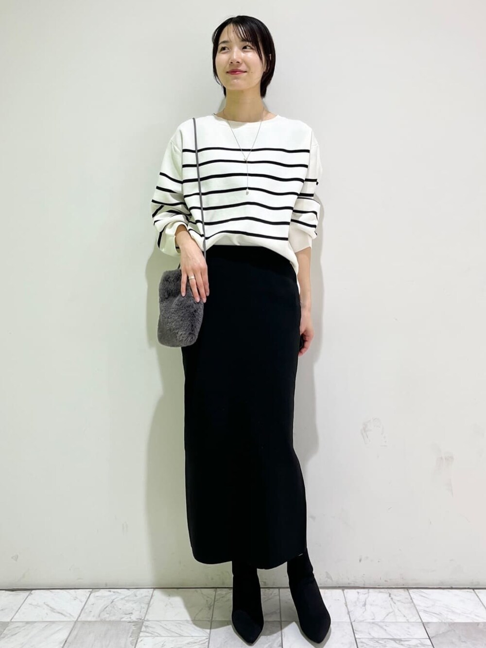 ホワイト系のニット/セーター、ブラック系のスカート、グレー系のショルダーバッグを着用したレディースの冬コーディネートの1枚目の写真