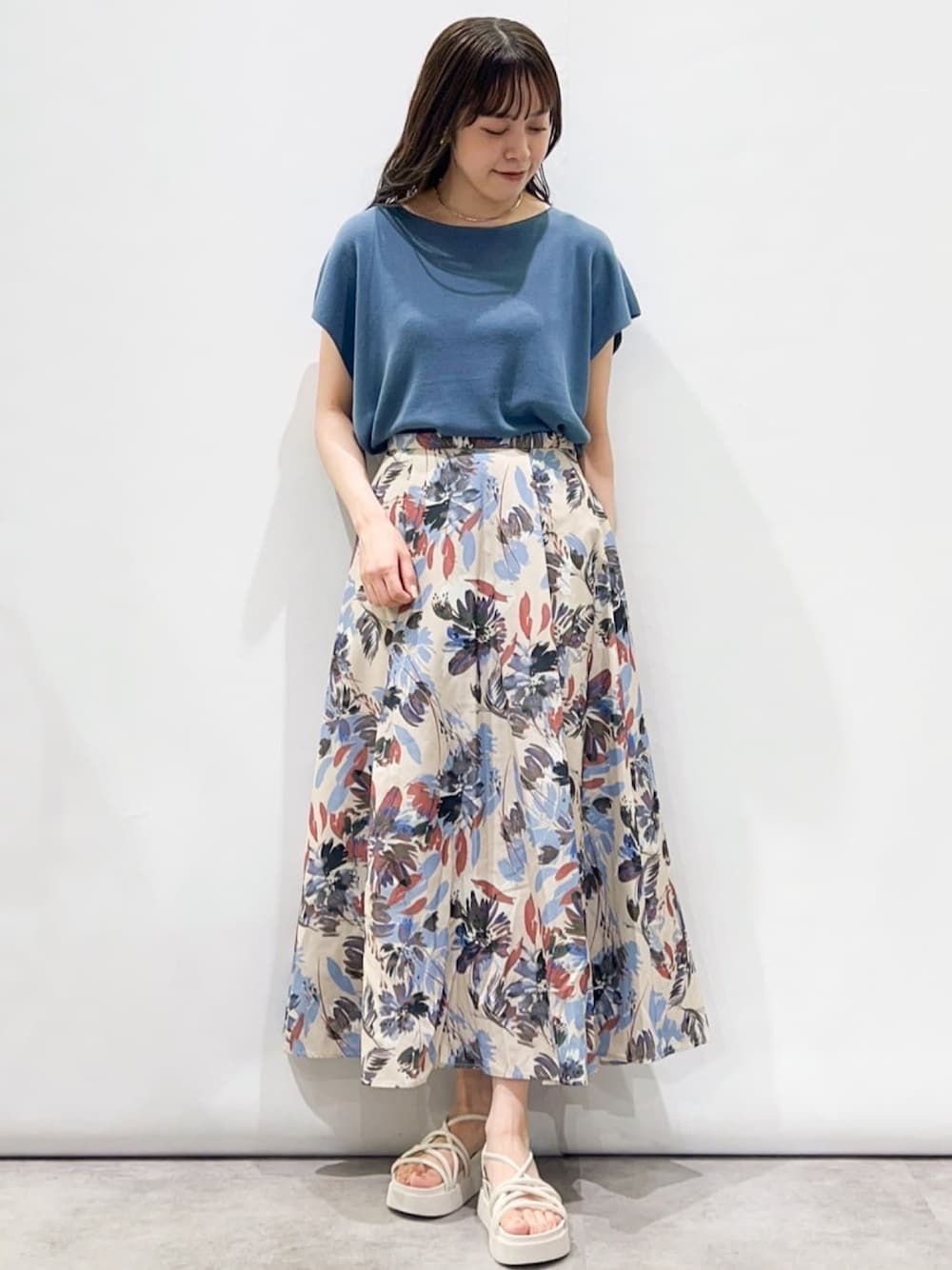 ブルー系のニット/セーター、ベージュ系のスカート、ホワイト系のサンダルを着用したレディースの夏コーディネートの1枚目の写真