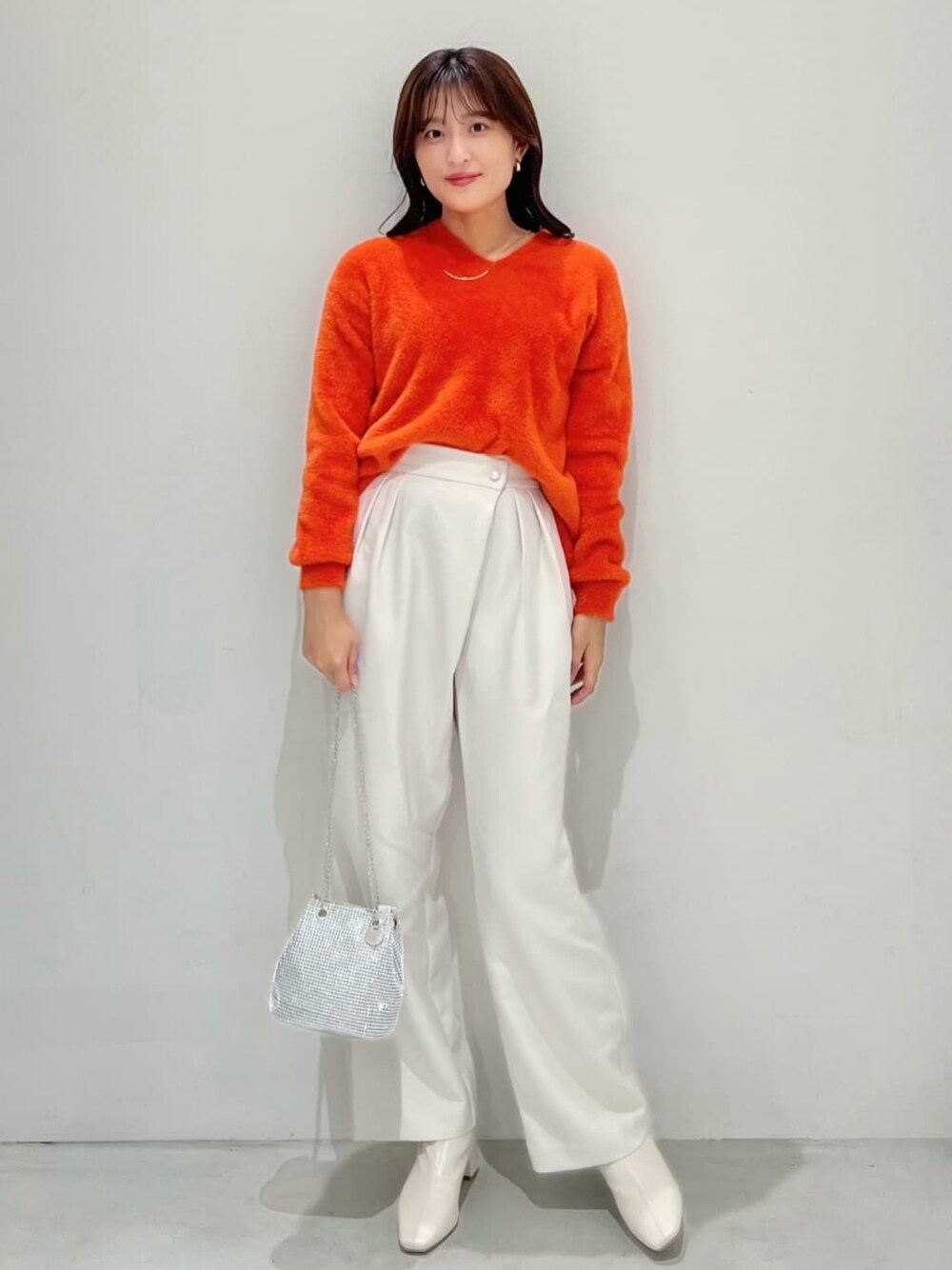 オレンジ系のニット/セーター、ホワイト系のその他パンツ、ホワイト系のショルダーバッグを着用したレディースの秋コーディネートの1枚目の写真