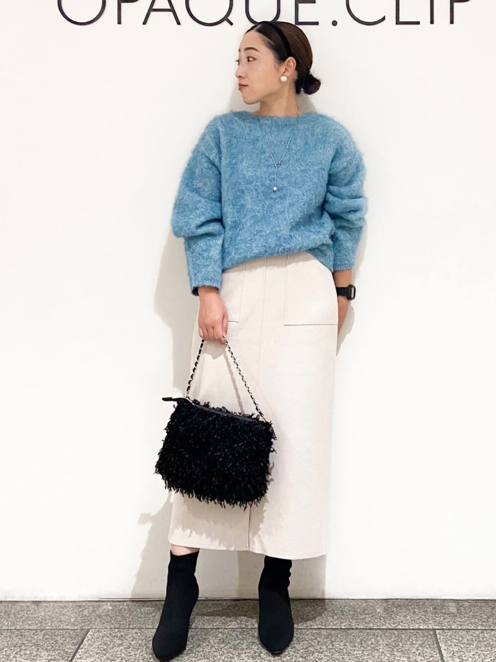 ブルー系のニット/セーター、ベージュ系のスカート、ブラック系のショルダーバッグを着用したレディースの冬コーディネートの1枚目の写真