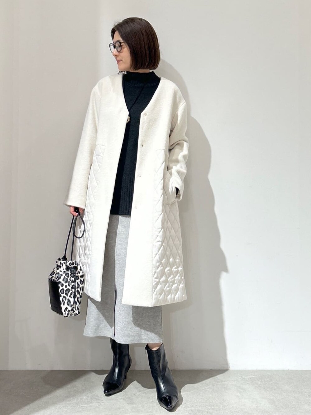ホワイト系のノーカラーコート、グレー系のスカート、ブラック系のショルダーバッグを着用したレディースの秋コーディネートの1枚目の写真