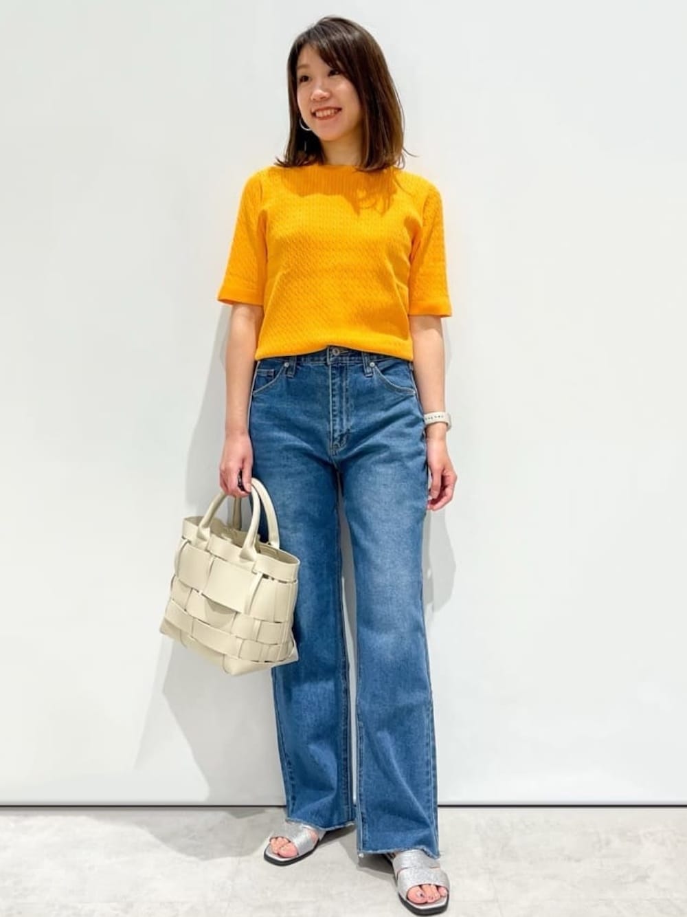 オレンジ系のニット/セーター、ブルー系のデニムパンツ、ホワイト系のトートバッグを着用したレディースの夏コーディネートの1枚目の写真