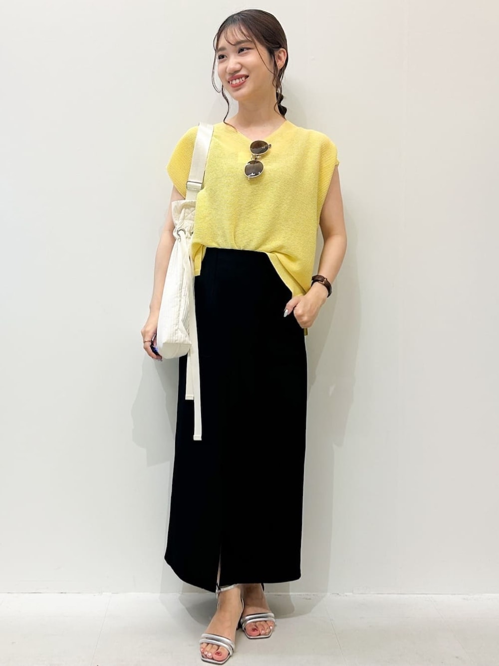 ブラック系のスカート、シルバー系のサンダル、イエロー系のニット/セーターを着用したレディースの夏コーディネートの1枚目の写真