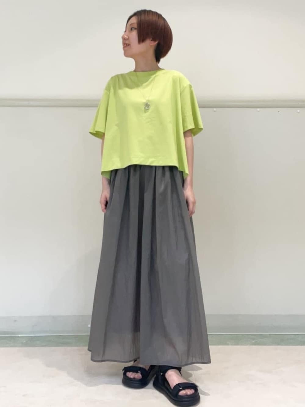グレー系のスカート、ブラック系のサンダル、グリーン系のTシャツ/カットソーを着用したレディースの春コーディネートの1枚目の写真