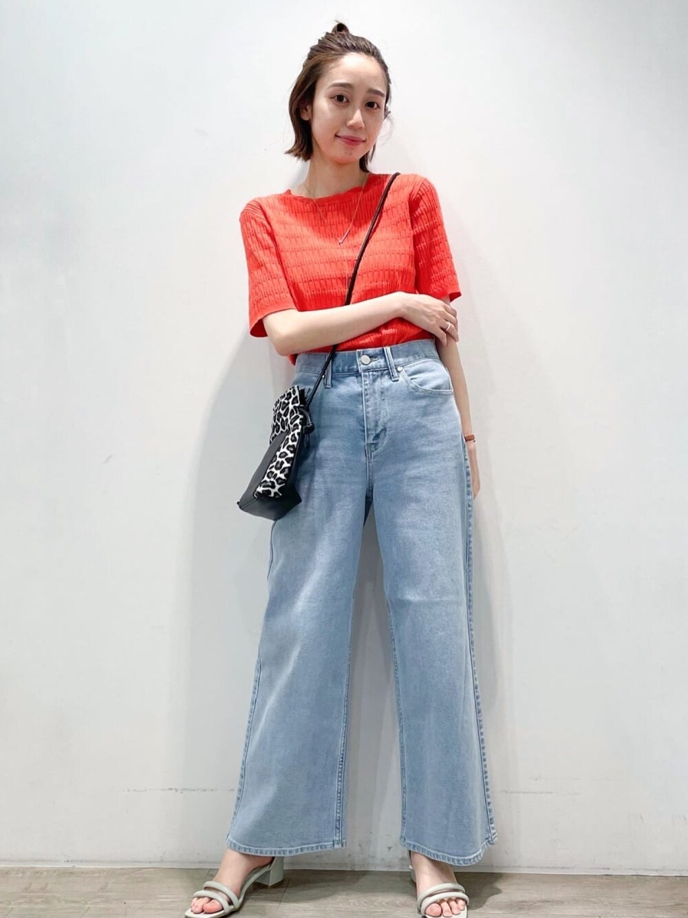 オレンジ系のニット/セーター、ブルー系のデニムパンツ、グリーン系のサンダルを着用したレディースの春コーディネートの1枚目の写真