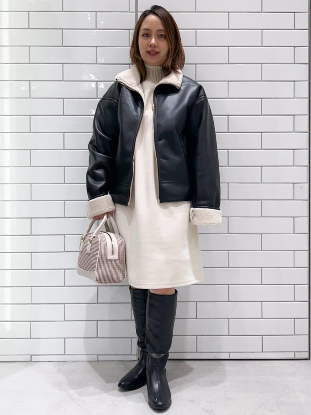 ブラック系のブルゾン、ホワイト系のワンピース、ブラック系のブーツを着用したレディースの冬コーディネートの1枚目の写真