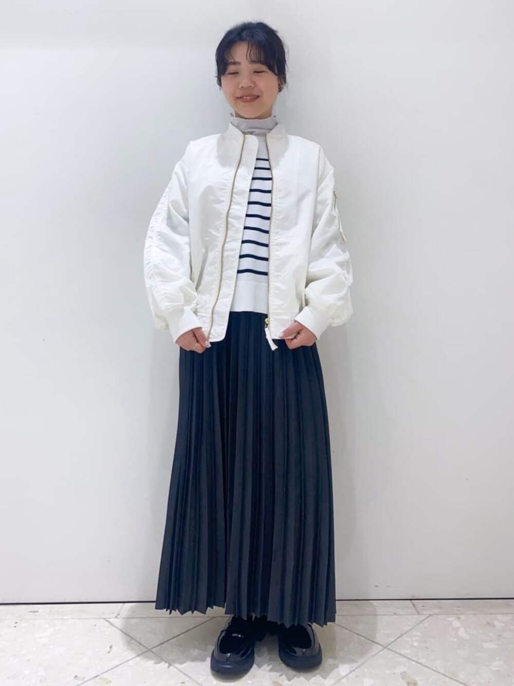 グレー系のスカート、ホワイト系のニット/セーター、ホワイト系のブルゾンを着用したレディースの冬コーディネートの1枚目の写真