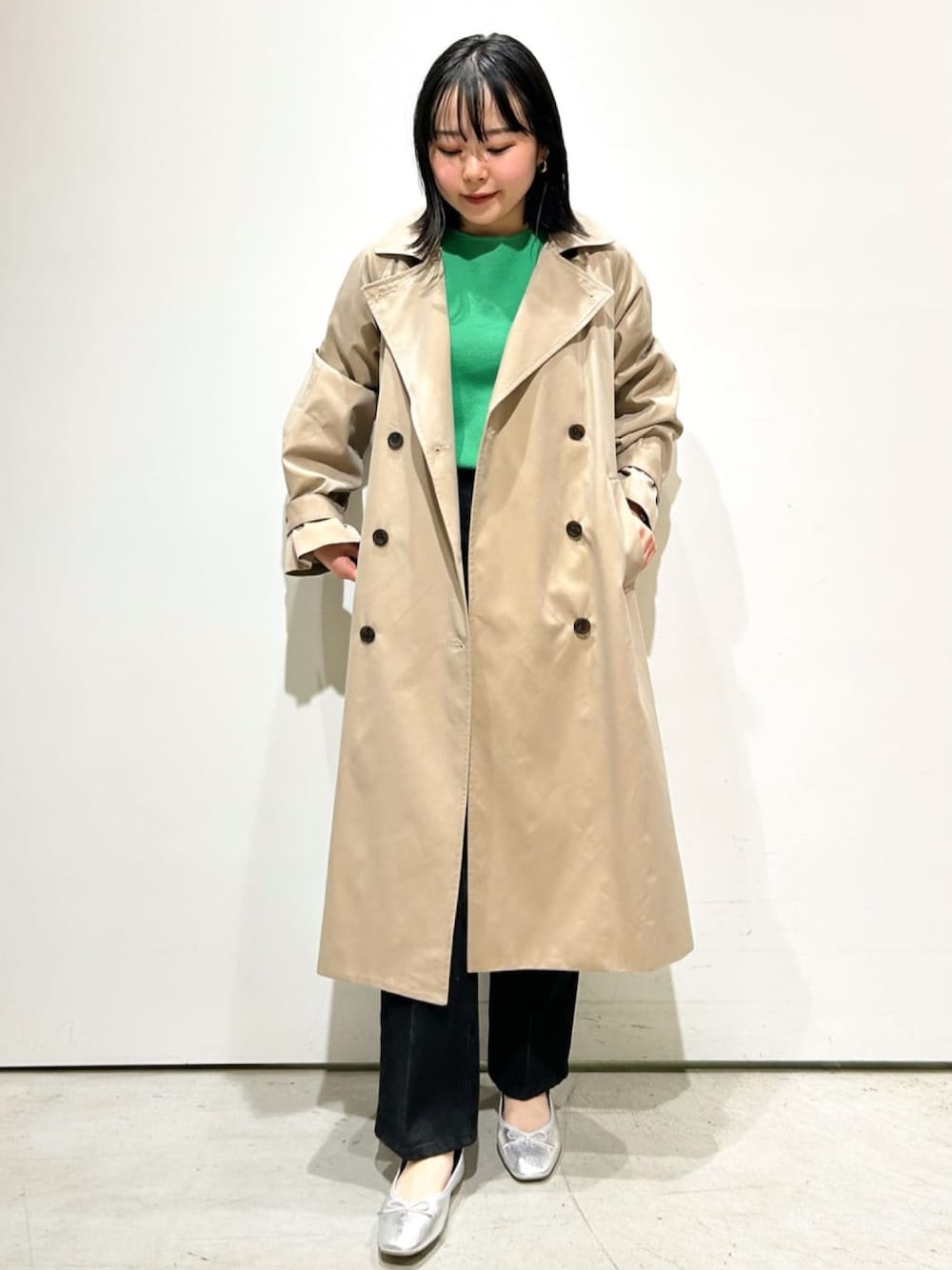 ベージュ系のトレンチコート、グリーン系のニット/セーター、グレー系のデニムパンツを着用したレディースの春コーディネートの1枚目の写真