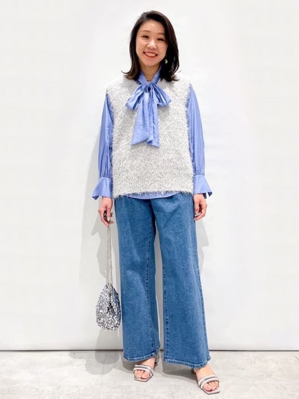 グレー系のベスト、ブルー系のシャツ/ブラウス、ブルー系のデニムパンツを着用したレディースの春コーディネートの1枚目の写真