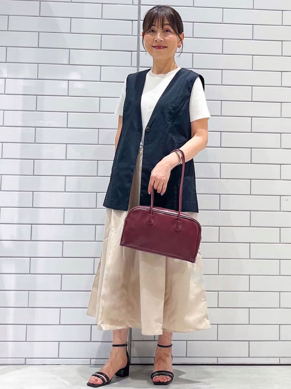 ブラック系のベスト、ベージュ系のワンピース、ブラック系のサンダルを着用したレディースの夏コーディネートの1枚目の写真