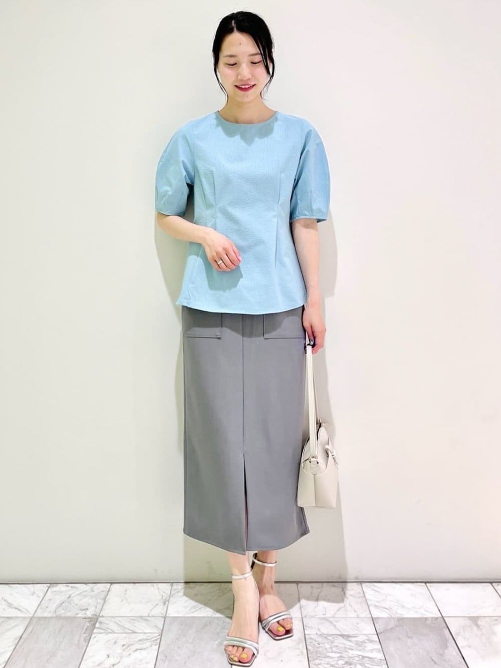 ブルー系のシャツ/ブラウス、グレー系のスカート、シルバー系のサンダルを着用したレディースの夏コーディネートの1枚目の写真