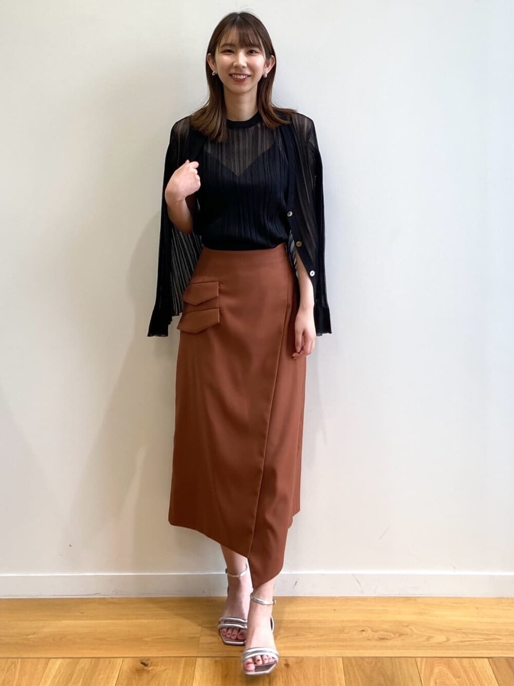 ブラウン系のスカート、シルバー系のサンダル、ブラック系のニット/セーターを着用したレディースの春コーディネートの1枚目の写真