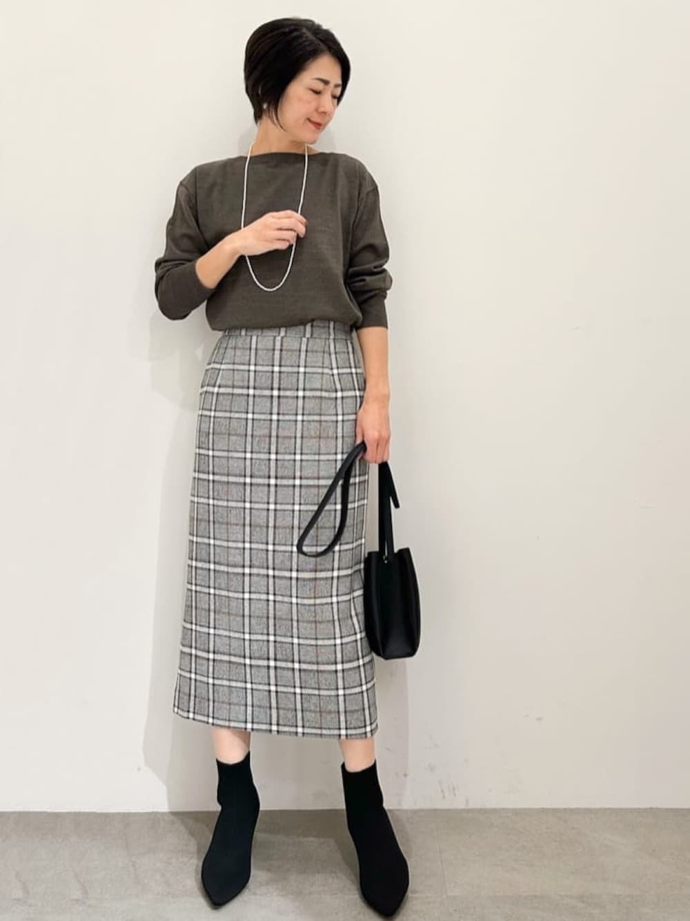 ブラック系のスカート、ブラック系のショルダーバッグ、ブラック系のブーツを着用したレディースの秋コーディネートの1枚目の写真