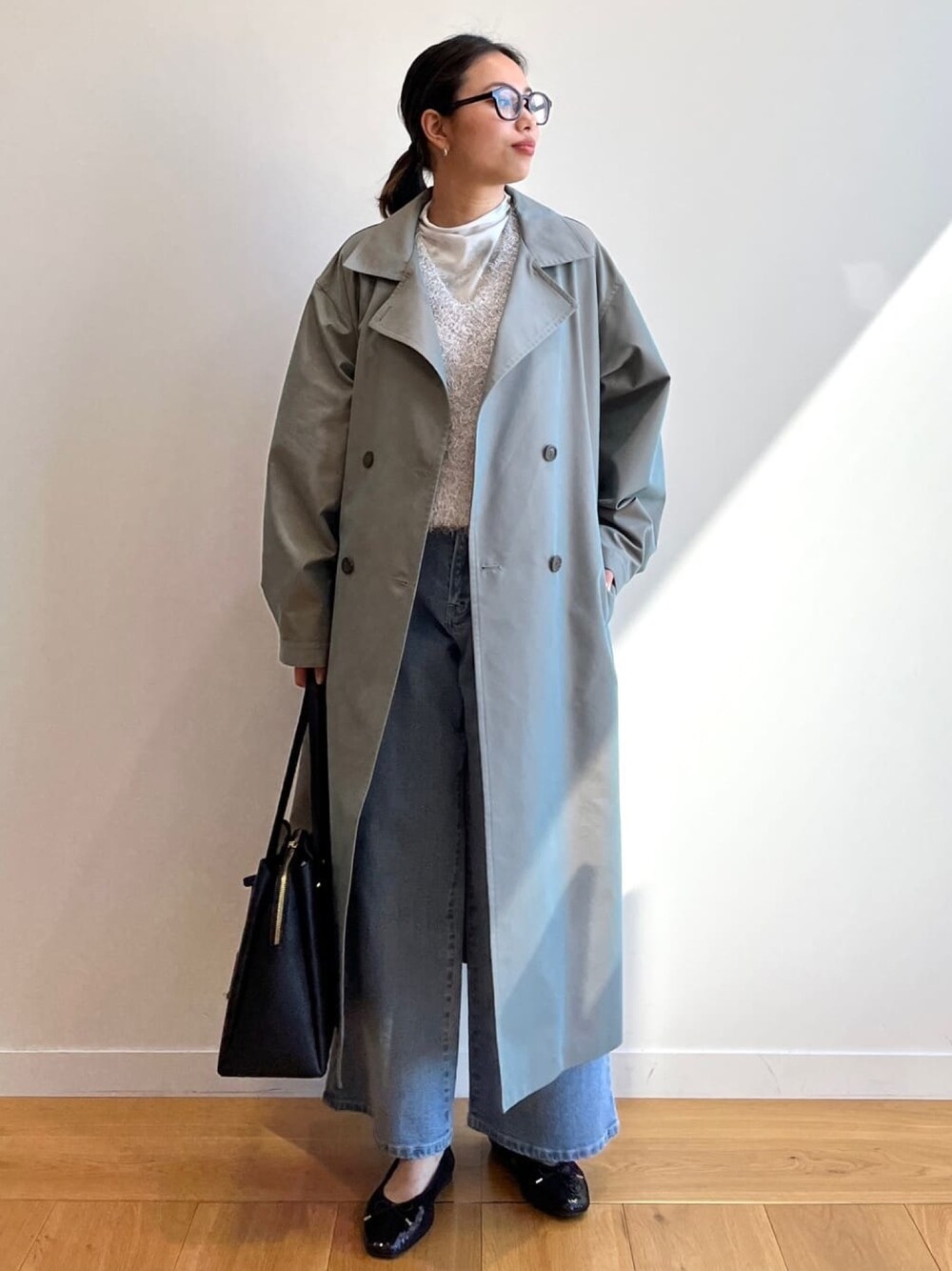 グリーン系のトレンチコート、ブルー系のデニムパンツ、ブラック系のトートバッグを着用したレディースの冬コーディネートの1枚目の写真