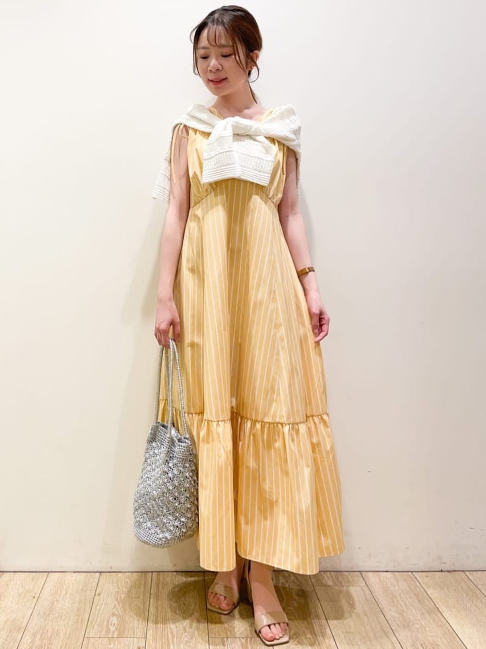 オレンジ系のワンピース、ホワイト系のカーディガン/ボレロ、シルバー系のトートバッグを着用したレディースの春コーディネートの1枚目の写真