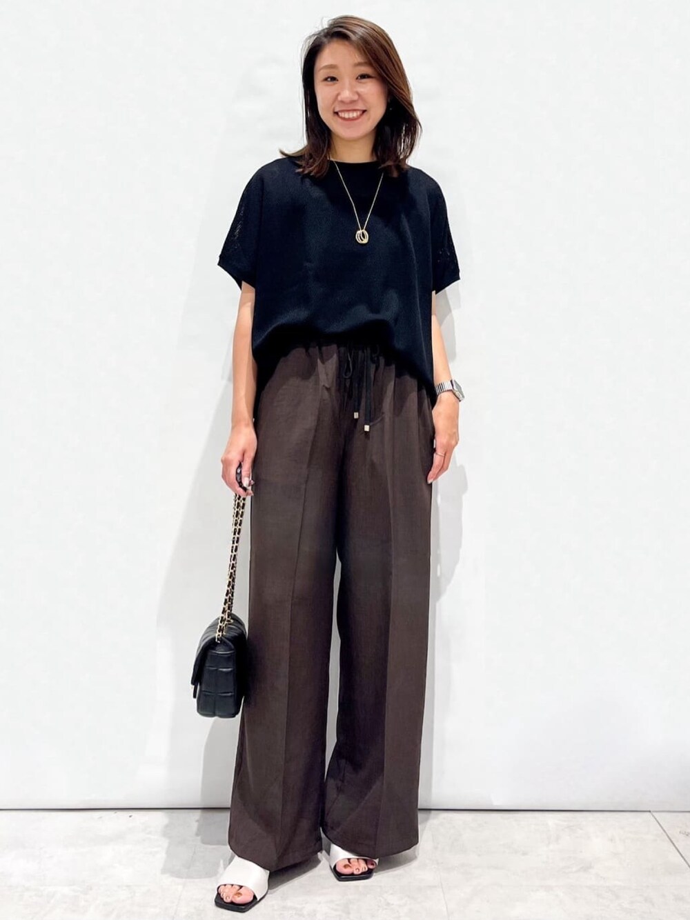 ブラウン系のその他パンツ、ホワイト系のサンダル、ブラック系のショルダーバッグを着用したレディースの夏コーディネートの1枚目の写真