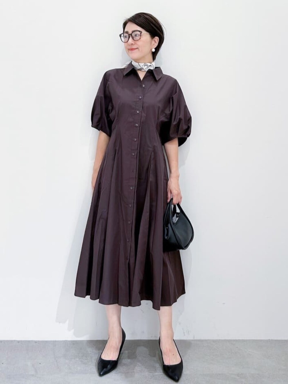 ブラウン系のワンピース、ブラック系のショルダーバッグ、ブラック系のパンプスを着用したレディースの夏コーディネートの1枚目の写真