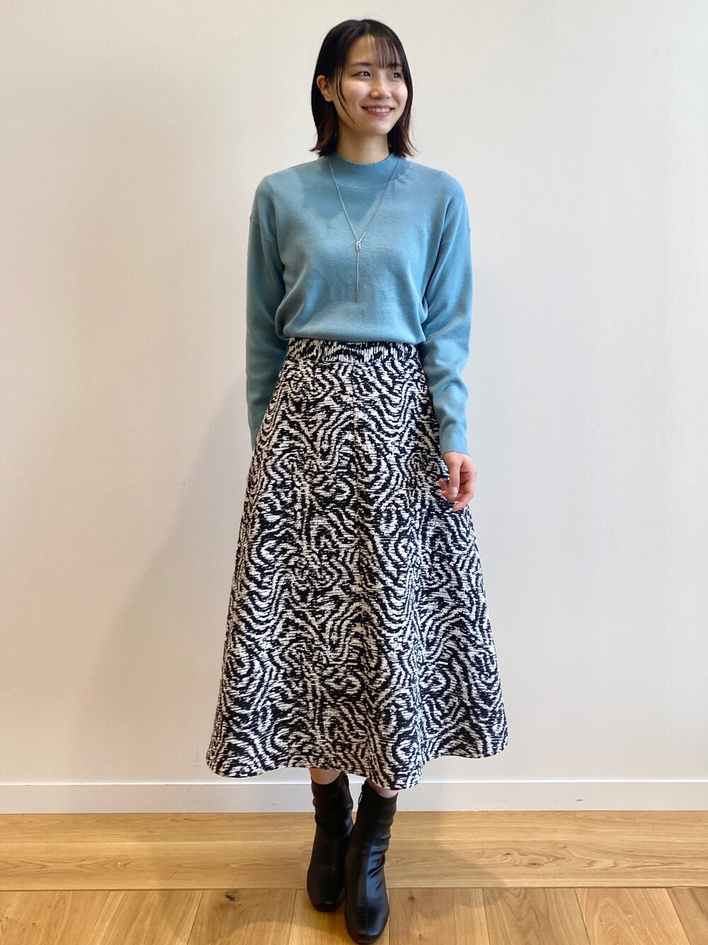 ブルー系のニット/セーター、ブラック系のスカート、ブラック系のブーツを着用したレディースの冬コーディネートの1枚目の写真