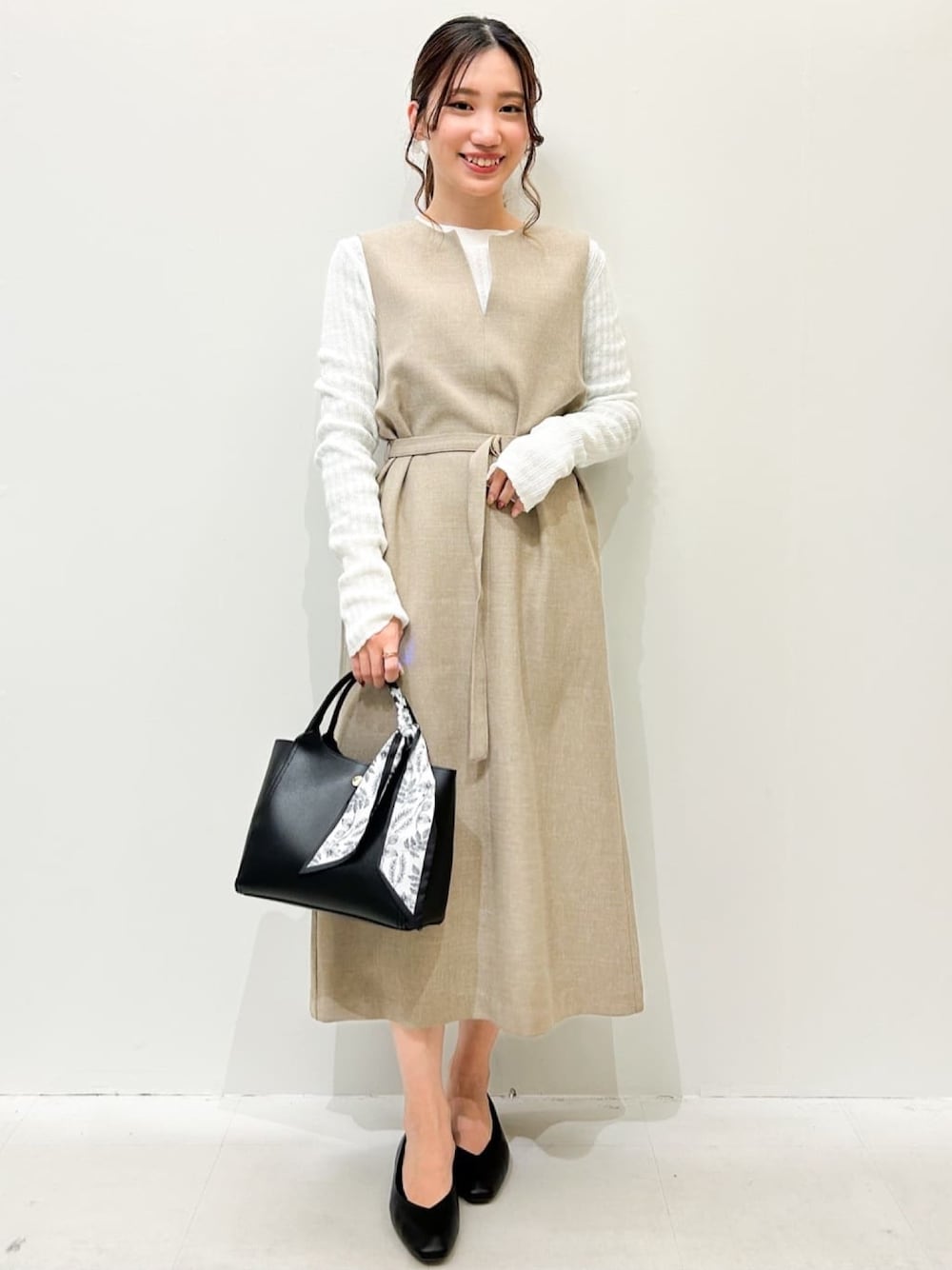 ベージュ系のワンピース、ホワイト系のニット/セーター、ブラック系のトートバッグを着用したレディースの春コーディネートの1枚目の写真