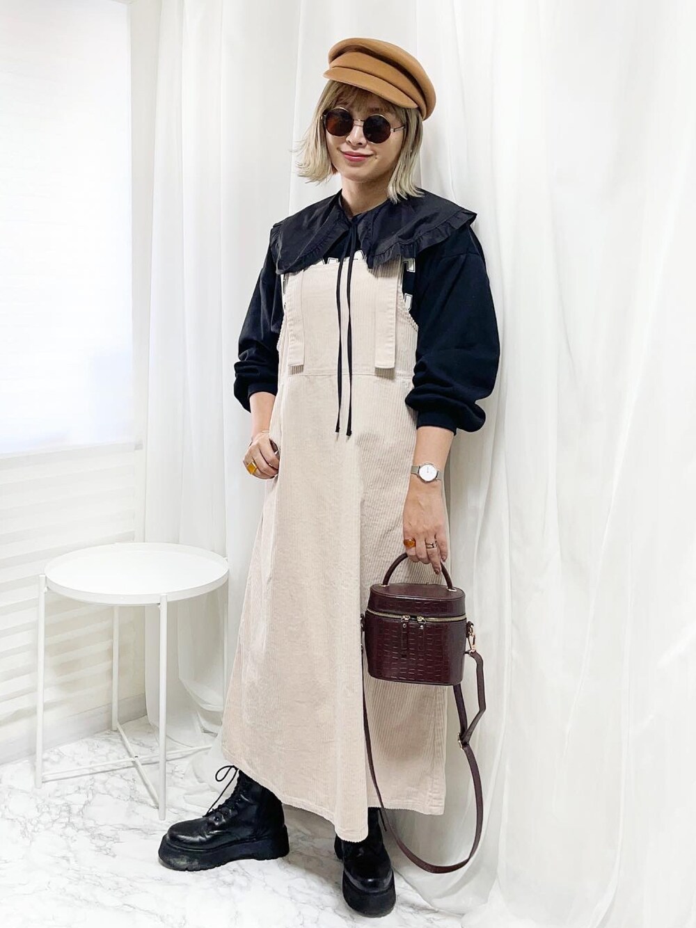 ブラウン系のショルダーバッグ、ブラック系のブーツ、ホワイト系のジャンパースカートを着用したレディースの春コーディネートの1枚目の写真