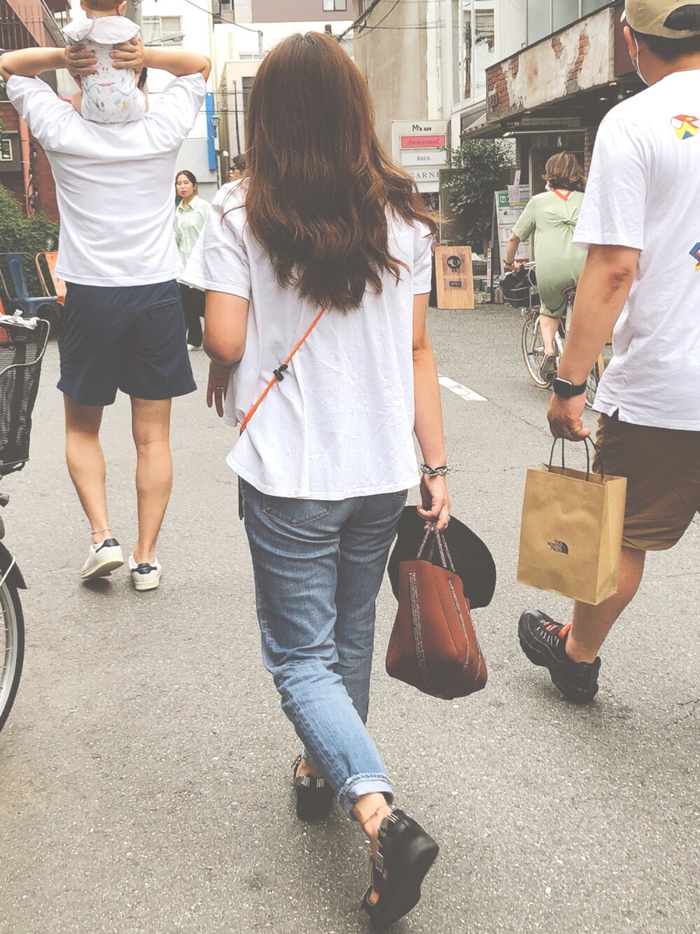 ブラウン系のハンドバッグ、ブラック系のサンダル、ホワイト系のTシャツ/カットソーを着用したレディースの秋コーディネートの1枚目の写真