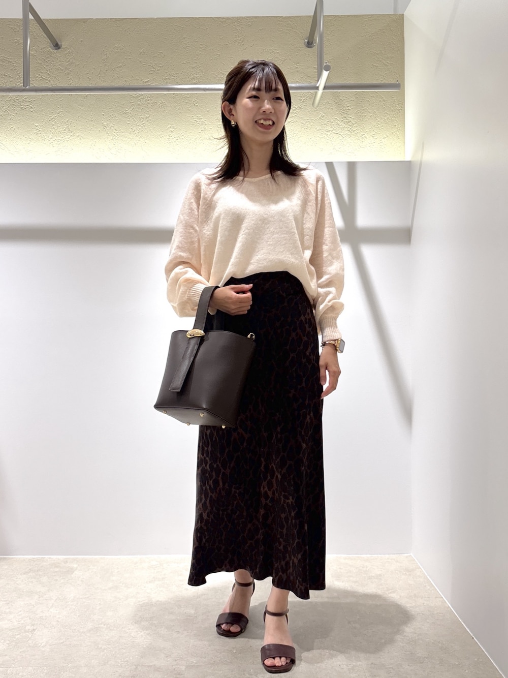 ベージュ系のニット/セーター、ブラウン系のスカート、ブラウン系のショルダーバッグを着用したレディースの夏コーディネートの1枚目の写真
