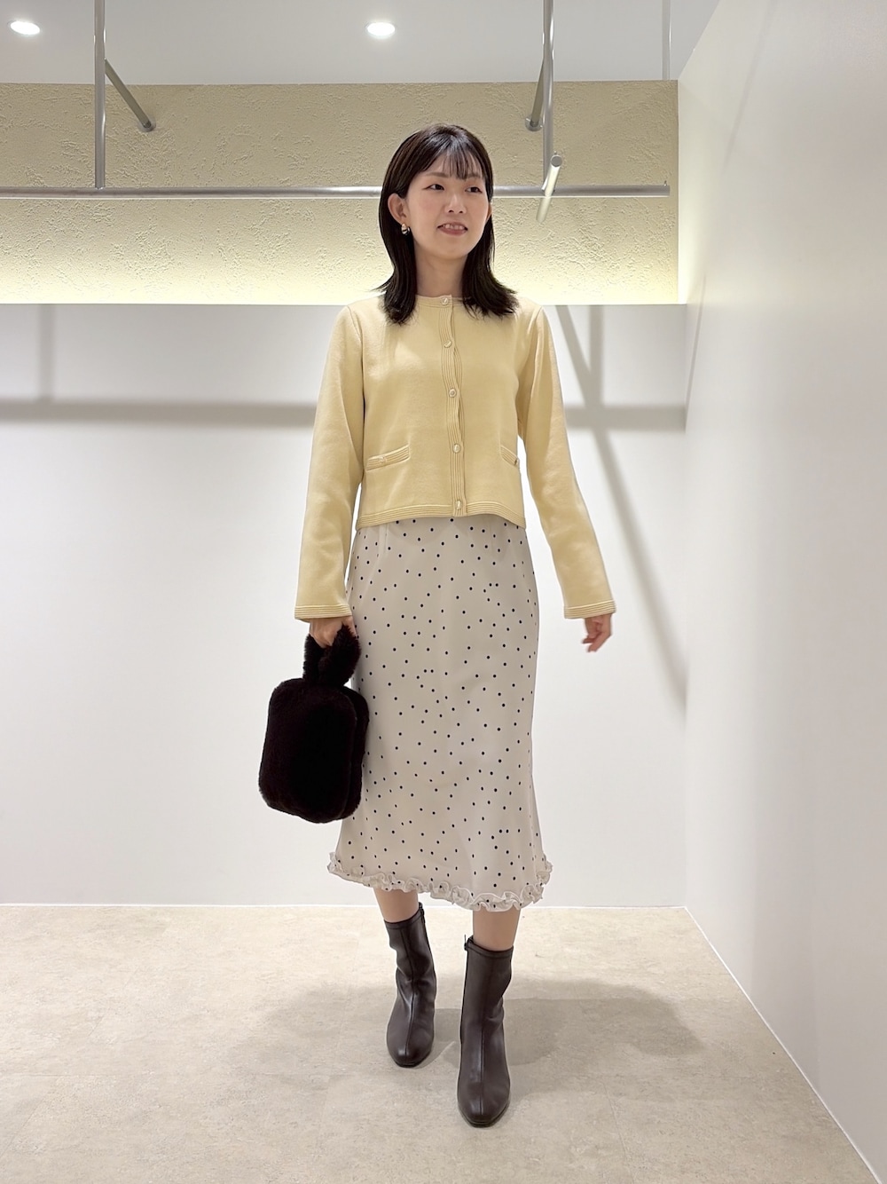 イエロー系のカーディガン/ボレロ、ホワイト系のスカート、ブラウン系のブーツを着用したレディースの秋コーディネートの1枚目の写真